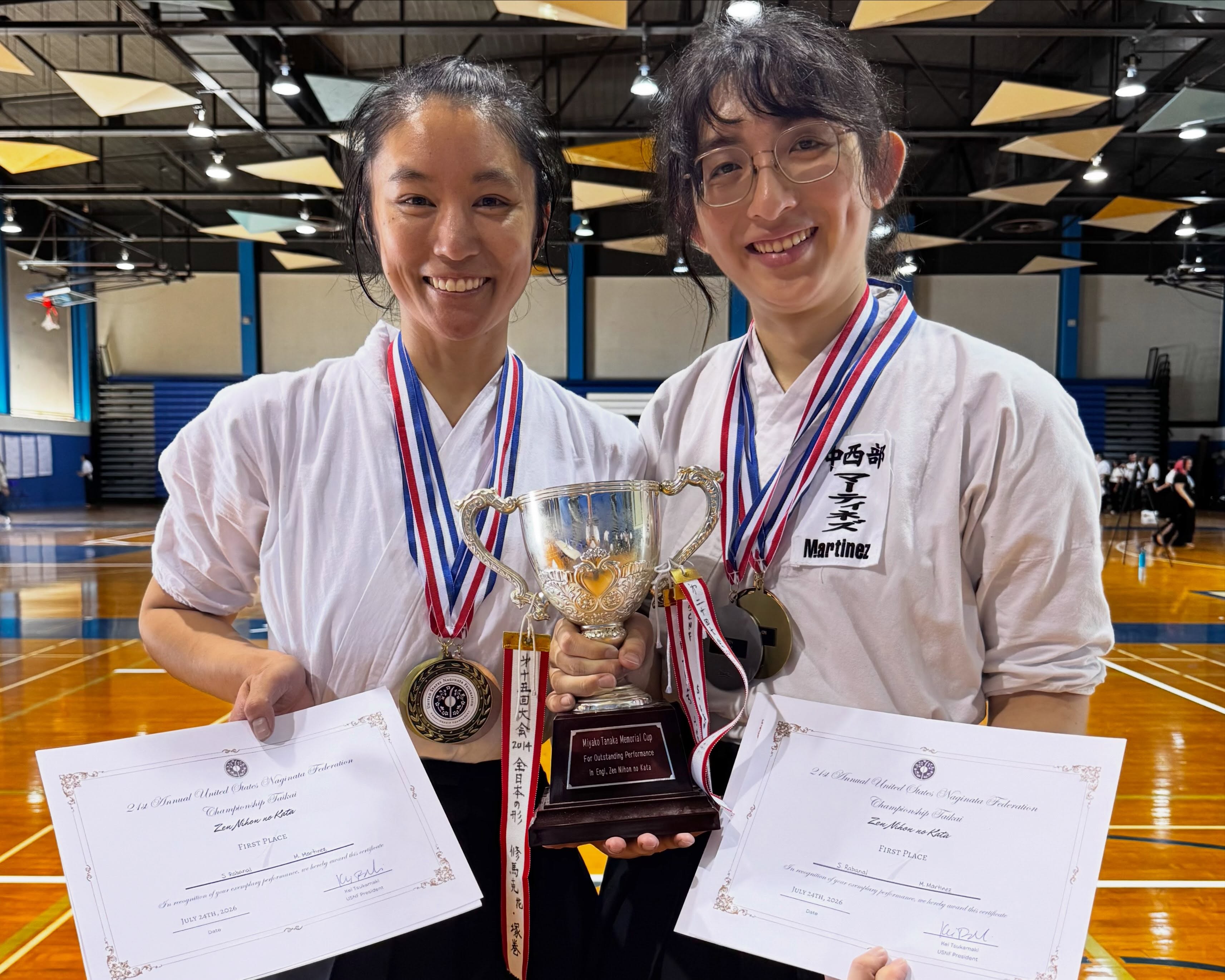Two people in martial arts uniform with many medals holding trophy